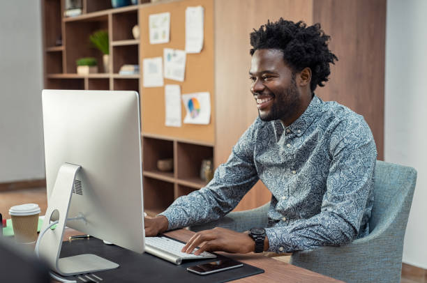 Portrait of african american businessman using computer at desk. Handsome employee enjoying work in modern office. Smiling creative business man feeling happy about positive report.