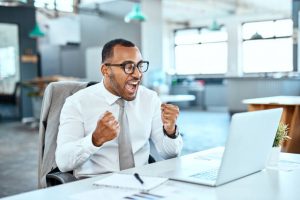 Shot of a young businessman cheering while working on a laptop in an office