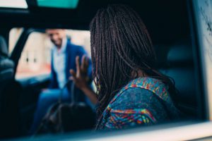 Man in suit holding bag and entering a car. African-American woman sitting in the back of the car.