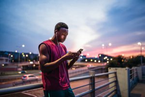 Young African men resting after training outdoors, in urban city environment, using mobile phone