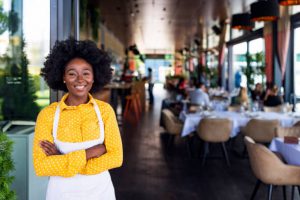 Young Female chef in apron standing with arms folded in restaurant.