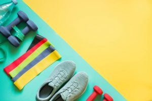 Sport and fitness equipment, rubber band, dumbbells, fitness shoes, measuring tape on punchy yellow. View from above, space for text.