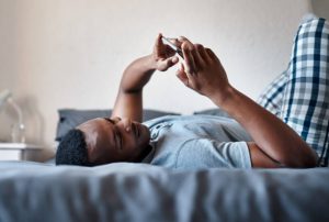 Cropped shot of a handsome young man lying down on his bed and using his cellphone while at home alone