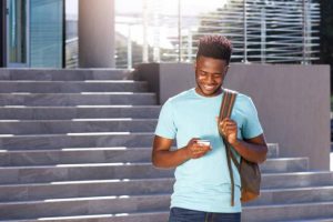 University student looking at his phone in front of a building