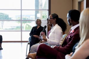 In answer to a question from the audience, the mid adult female panel member gestures and uses the microphone.