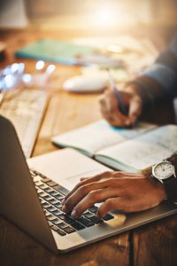 Cropped shot of a man using a laptop and notebook to make an organized schedule