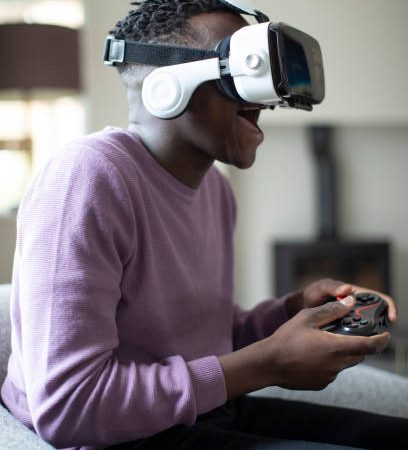 Excited Teenage Boy Playing Video Game At Home Wearing Virtual Reality Headset