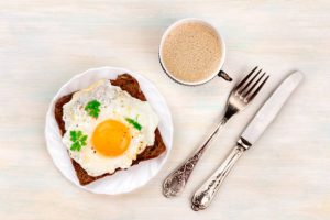 A plate with a sunny side up fried egg on a bread toast with coffee, a fork, and a knife.