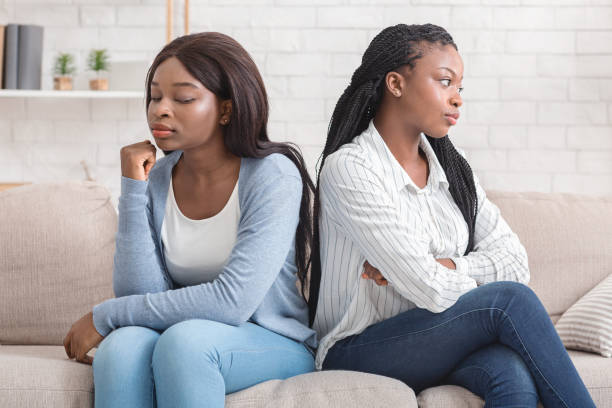 Offended black girlfriends sitting back to back on couch, ignoring each other after quarrel at home