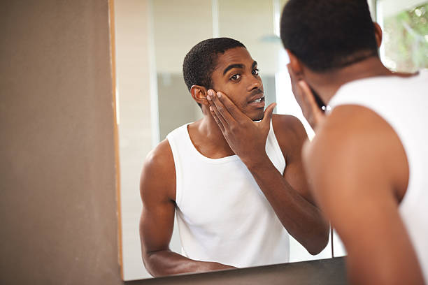 A young man applying cream to his face while looking in the mirror