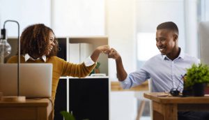 Shot of two young work colleagues greeting each other with a fist pump while being seated in the office