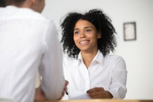 Smiling African female HR employer interviewing male job applicant asking questions.