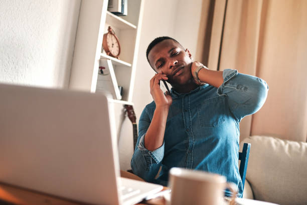 Cropped shot of a handsome young businessman sitting and using his cellphone at home while suffering from neck ache