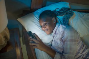 happy Afro American millennial woman as social media addict - night lifestyle portrait of young beautiful and cool girl texting or online dating on mobile phone in bed smiling cheerful