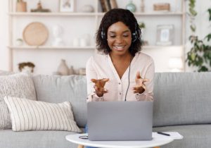 A young lady smiling at her laptop with her headphones on