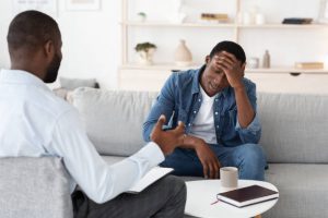 Depressed black man talking to psychologist during individual therapy, therapist advising something
