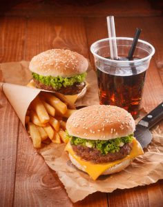 Two hamburgers and fries on brown paper with glass of soft drink