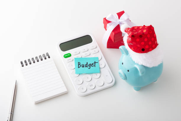 Piggy bank wearing Christmas hat with word budget on calculator and notepad with pen, christmas saving and budget concept