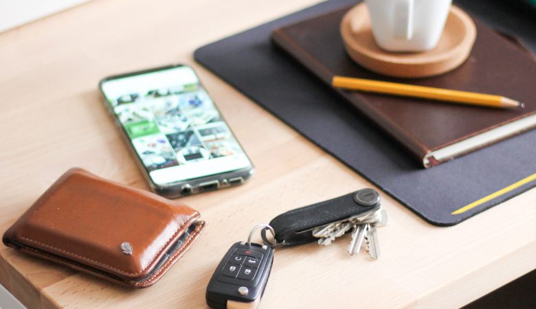An image of a wallet, a phone, a bunch of keys and a car remote, a cup of tea on a saucer, a notebook and more, on a table.