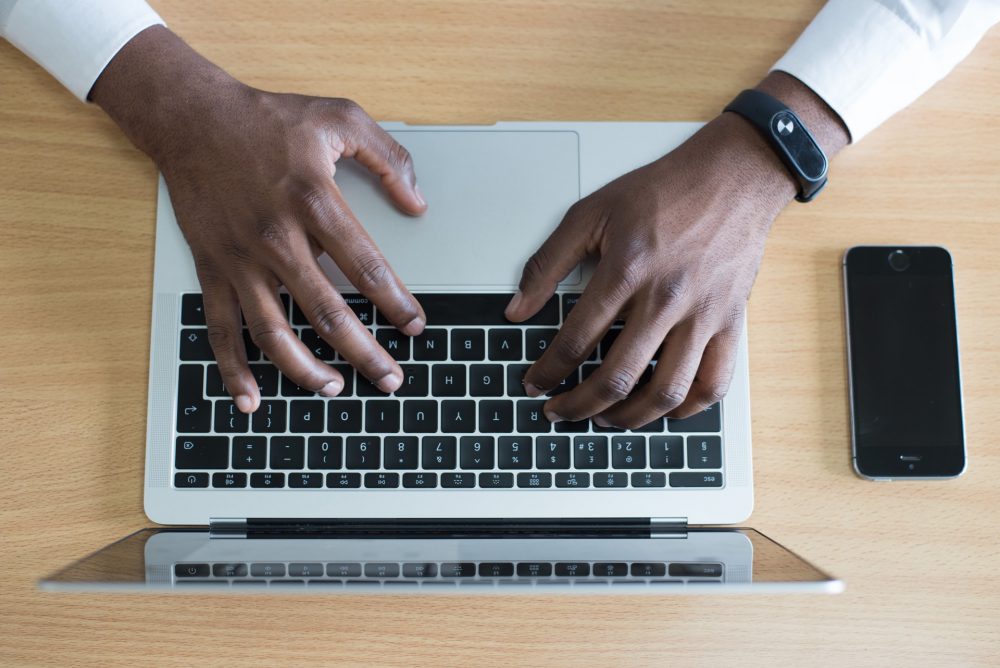 Hands typing on a laptop keyboard, with a phone on the side