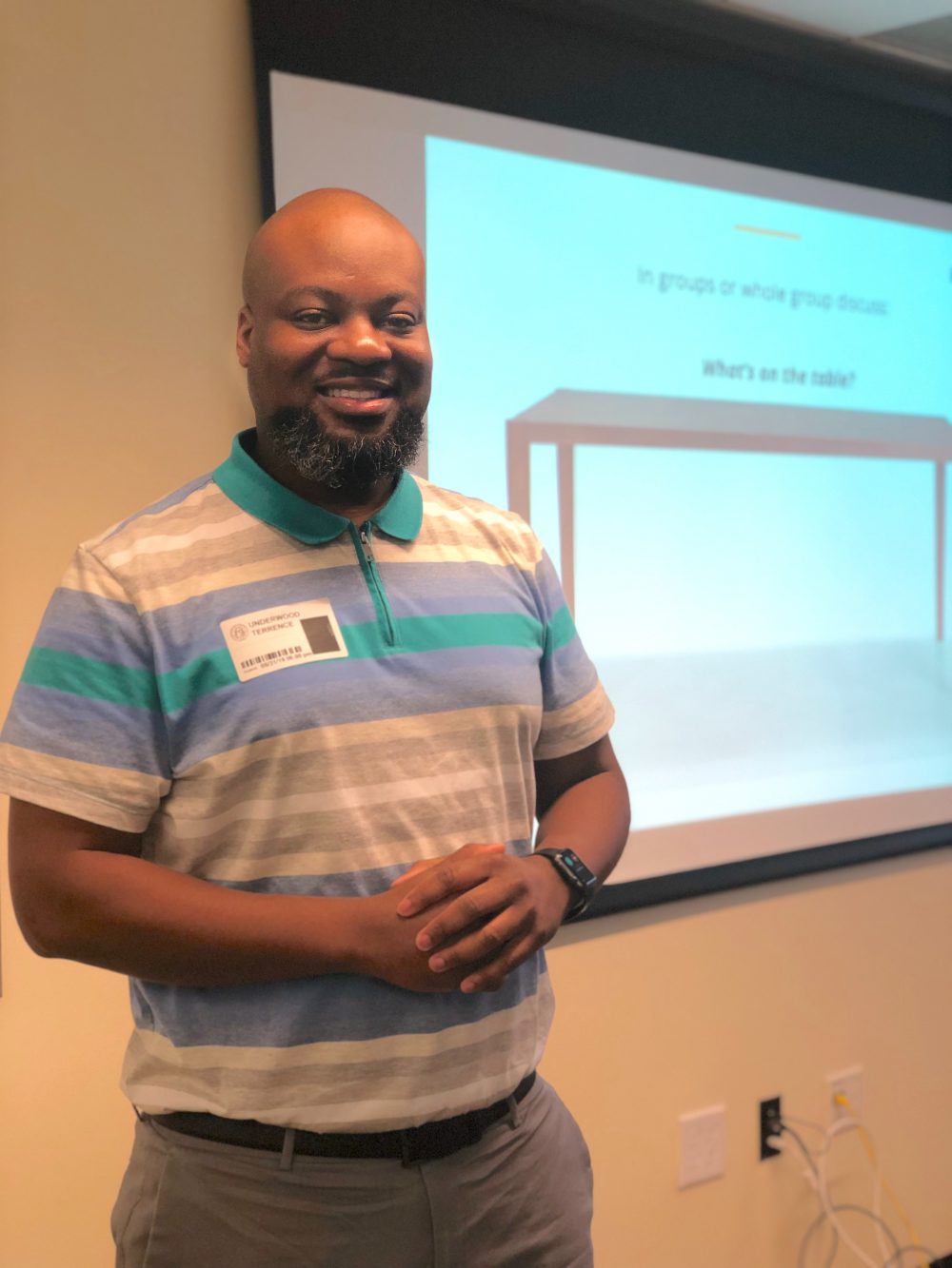 A male lecturer smiling and standing next to an electric teaching board