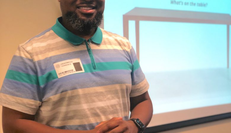 A male lecturer smiling and standing next to an electric teaching board