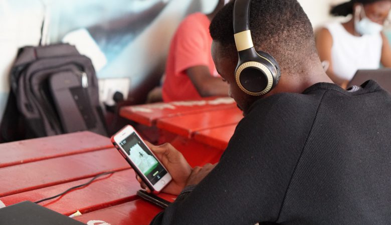 A young man at a table using holiding his phone and using headphones